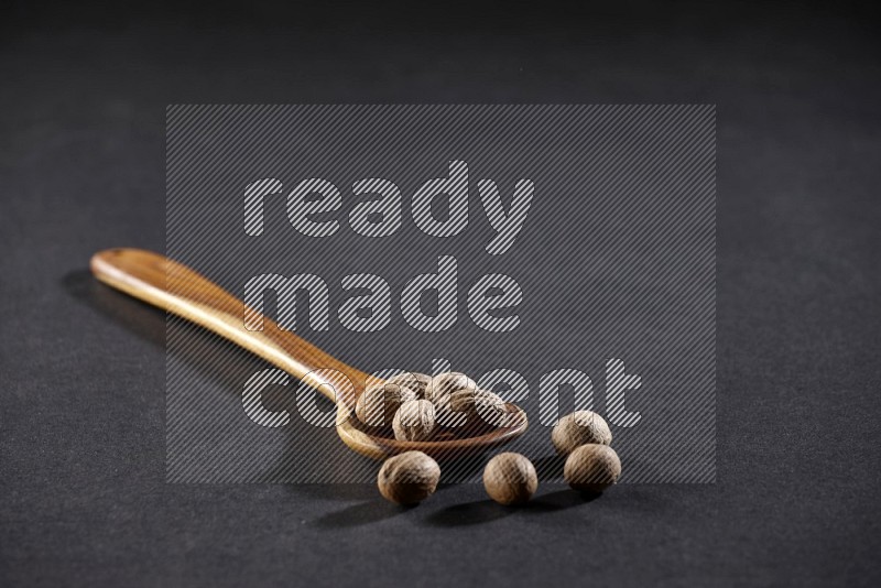 A wooden ladle full of nutmeg on a black flooring in different angles