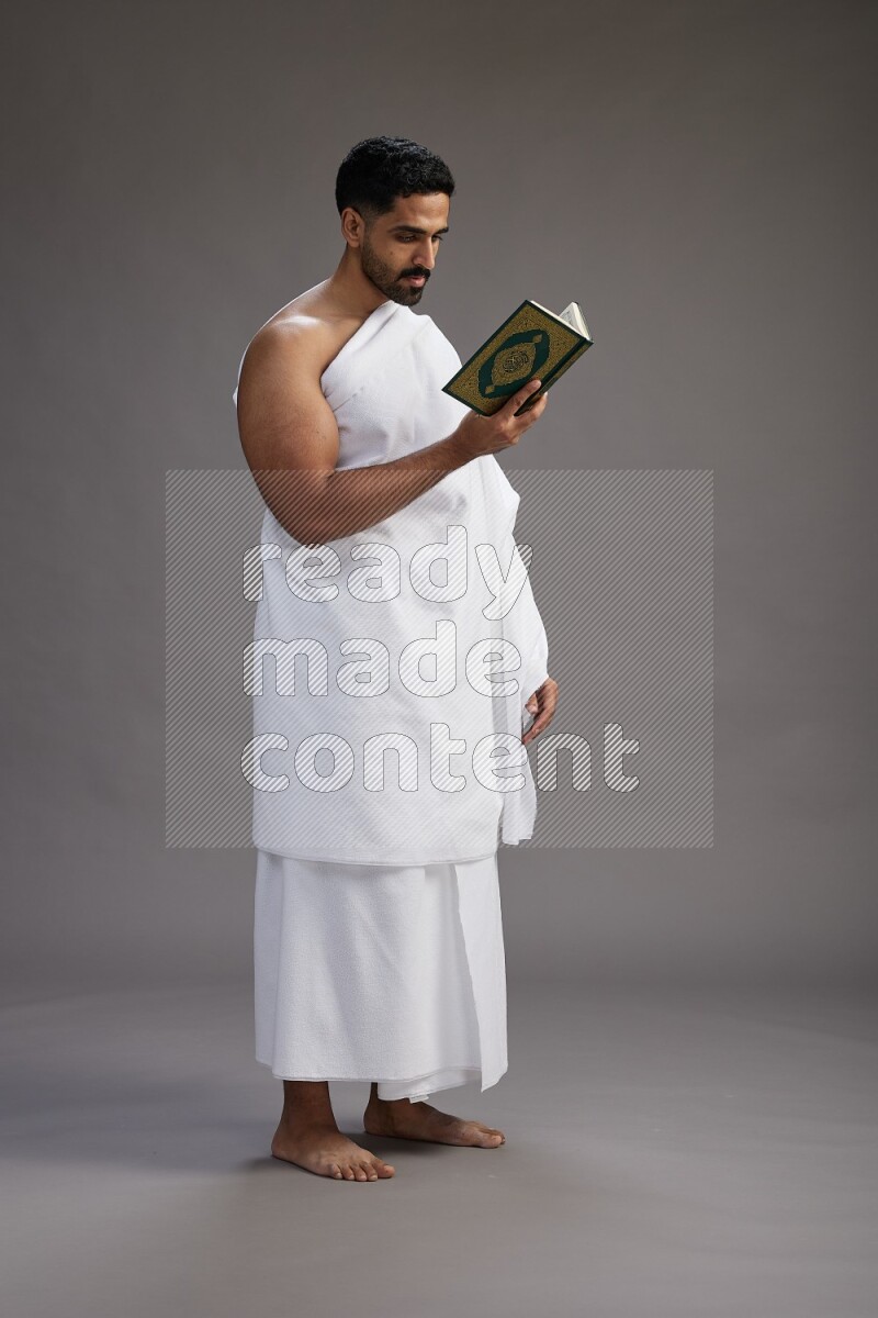 A man wearing Ehram Standing reading quran on gray background