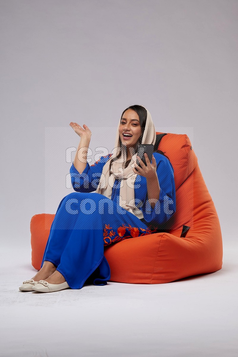 A Saudi woman sitting on an orange beanbag and texting on phone