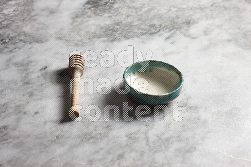 Multicolored Pottery bowl with wooden honey handle on the side with grey marble flooring, 45 degree angle