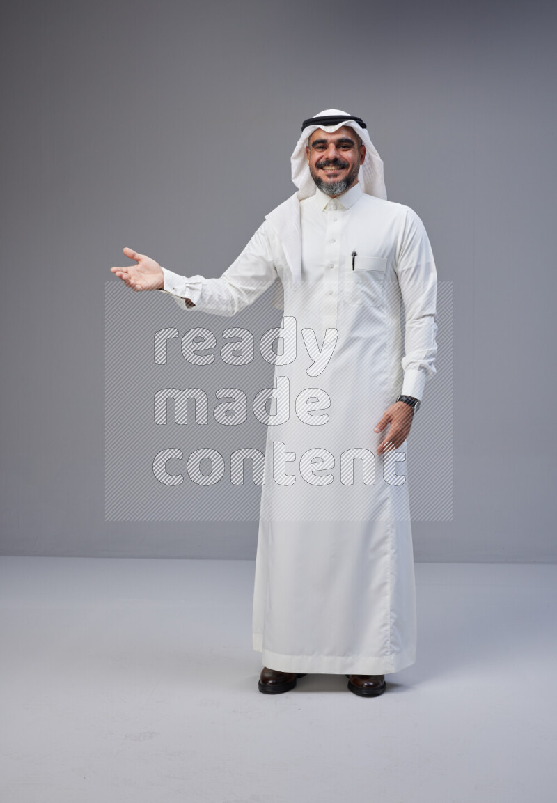 Saudi man Wearing Thob and white Shomag standing interacting with the camera on Gray background