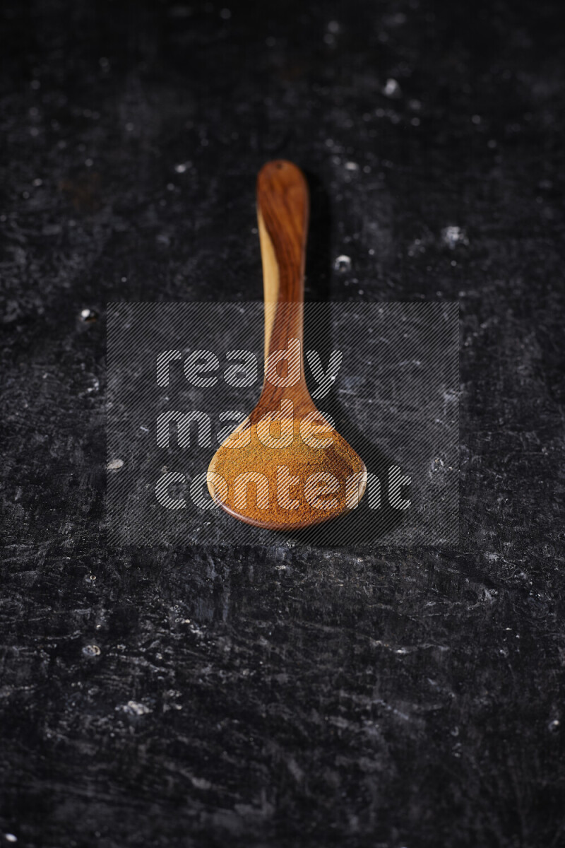 A wooden ladle full of ground paprika powder on black background