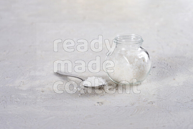 A glass jar full of coarse sea salt crystals on white background