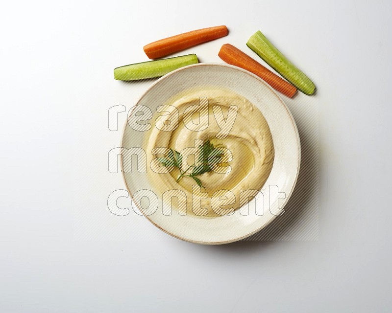 Hummus in a pottry plate garnished with parsley on a white back ground