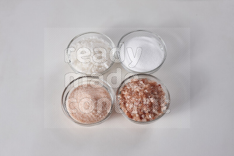 4 glass bowls filled with table salt, coarse sea salt, fine himalayan salt and coarse himalayan salt on white background