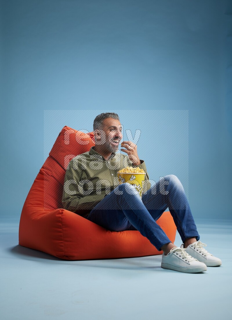 A man sitting on an orange beanbag and eating popcorn