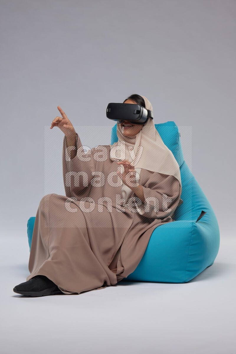 A Saudi woman sitting on a blue beanbag and gaming with VR