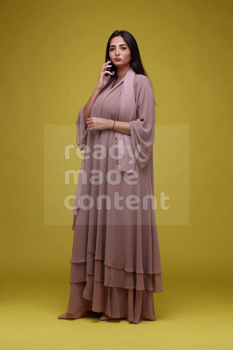A woman Calling on a Yellow Background wearing Brown Abaya