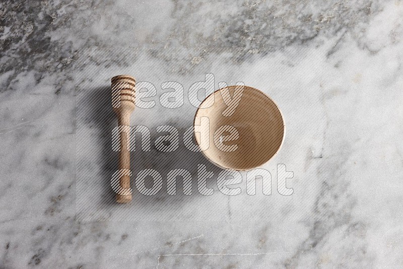 Beige Pottery bowl with wooden honey handle on the side with grey marble flooring, 65 degree angle