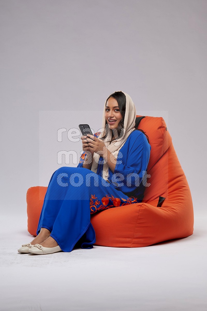 A Saudi woman sitting on an orange beanbag and texting on phone