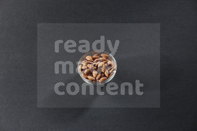 A glass bowl full of peeled almonds on a black background in different angles