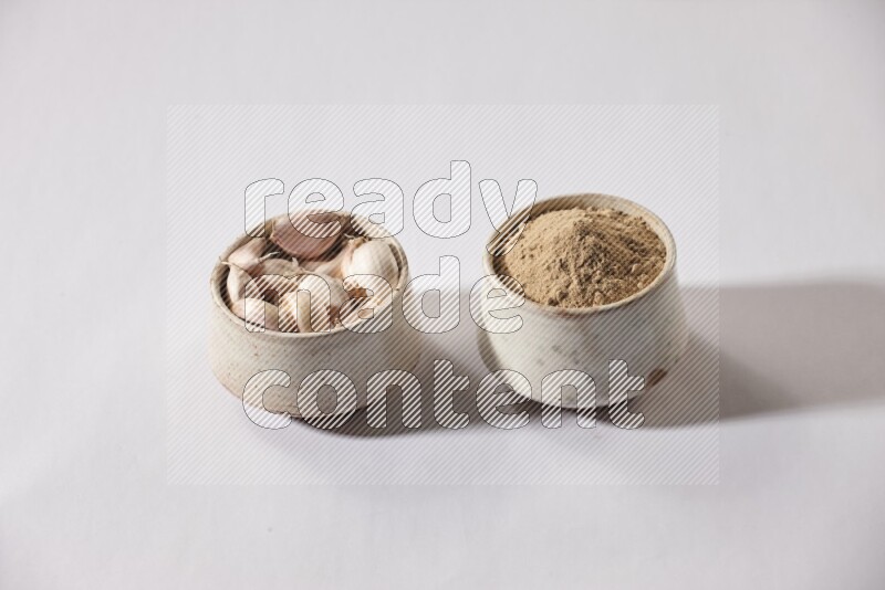 2 beige pottery bowls, one full of garlic powder and the other full of garlic cloves on a white flooring