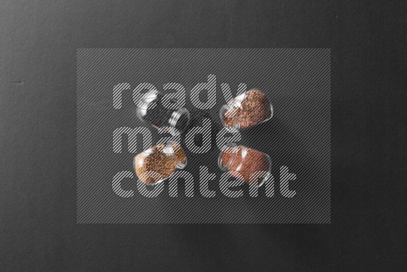 4 glass spice jars full of black seeds, mustard seeds, flax and garden cress on black flooring