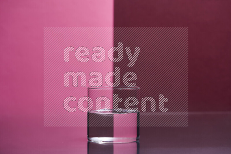 The image features a clear glassware filled with water, set against pink and dark red background