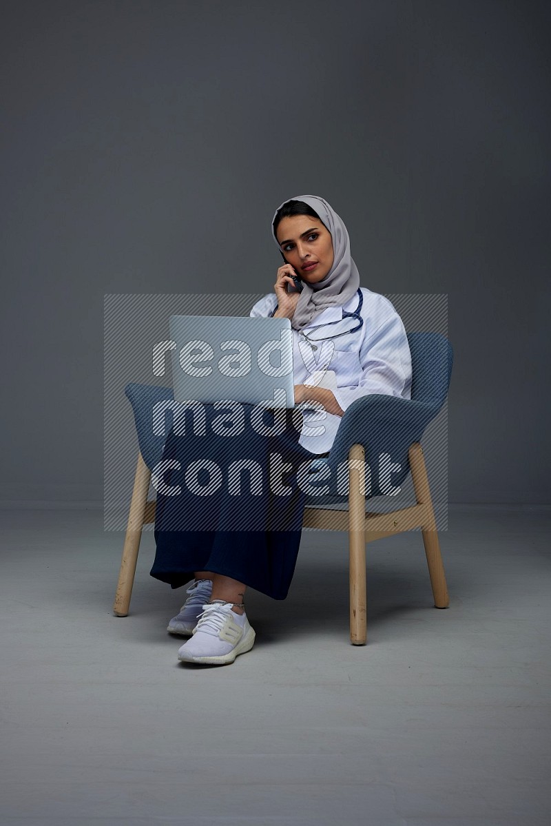 A doctor wearing a light gray head scarf sitting on blue chair on grey background