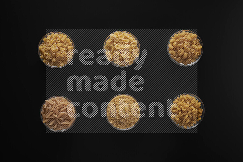 Different pasta types in 6 glass bowls on black background