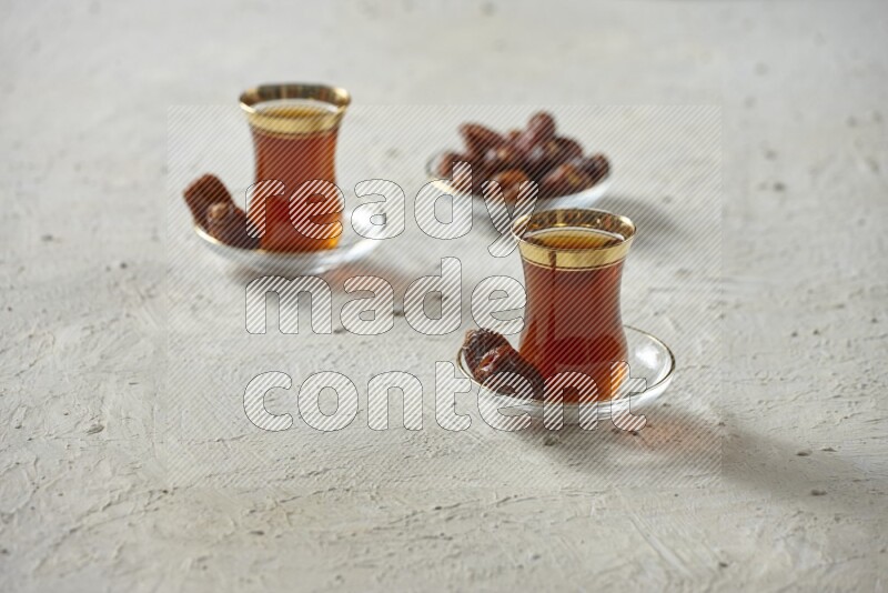 A tea glass cup with dates and coffee on textured white background