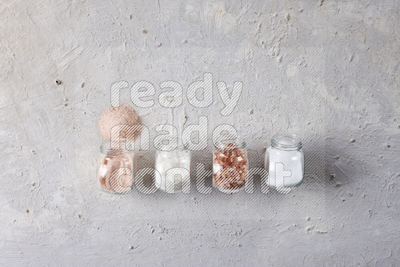 4 glass jars filled with table salt, coarse sea salt, fine himalayan salt and coarse himalayan salt on white background