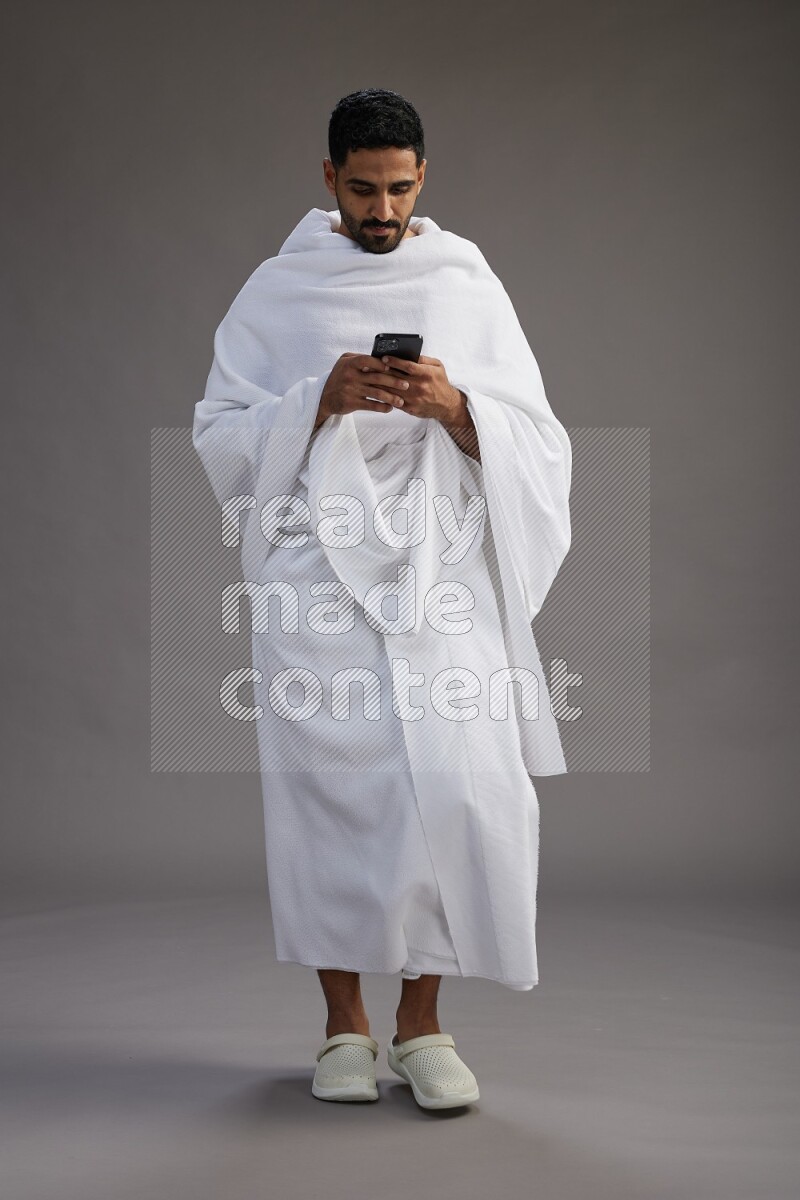 A man wearing Ehram Standing texting on phone on gray background