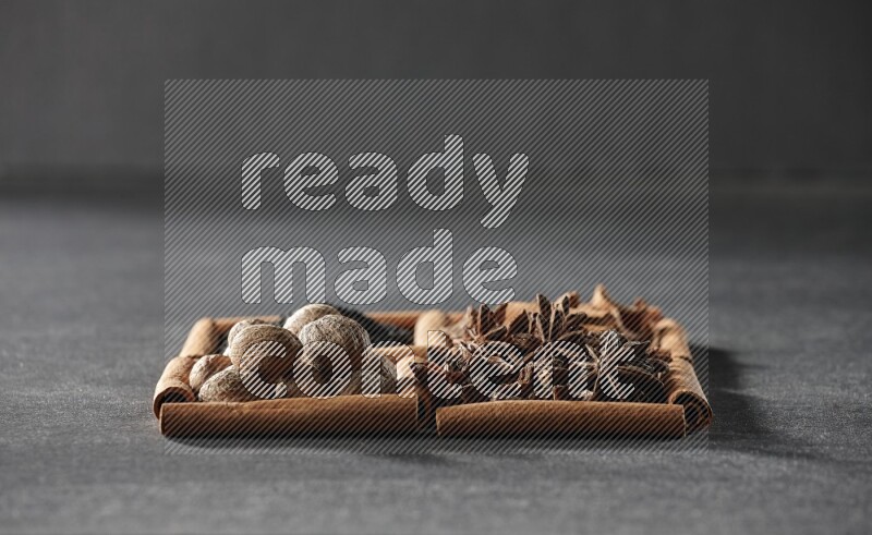 4 مربعات من عيدان القرفة ممتلئة بحبة البركة السوداء والقرفة واليانسون النجمي وجوزة الطيب على أرضية سوداء