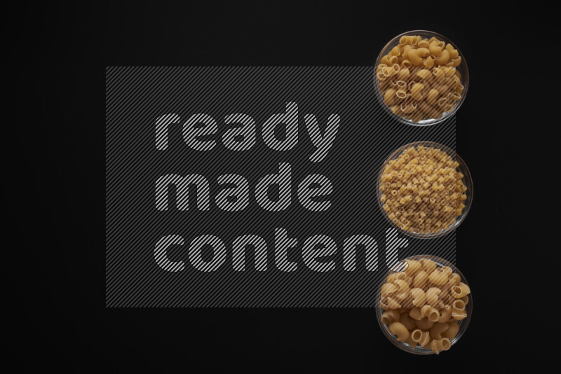 Different pasta types in 3 glass bowls on black background