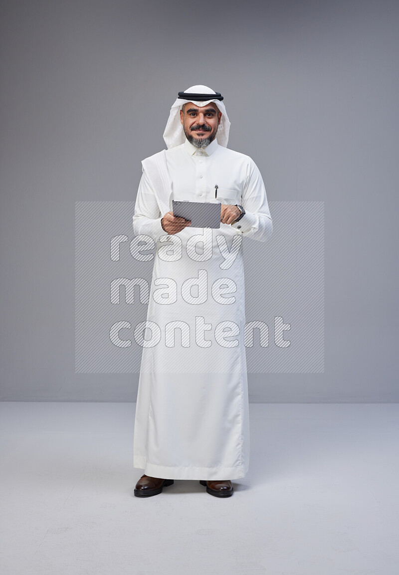 رجل سعودي يرتدي ثوب وشماغ ابيض يحمل تابلت ويتفاعل امام الكاميرا
