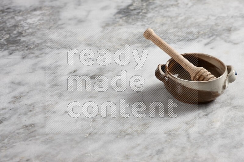 Multicolored pottery bowl with wooden honey dipper in it on grey marble background