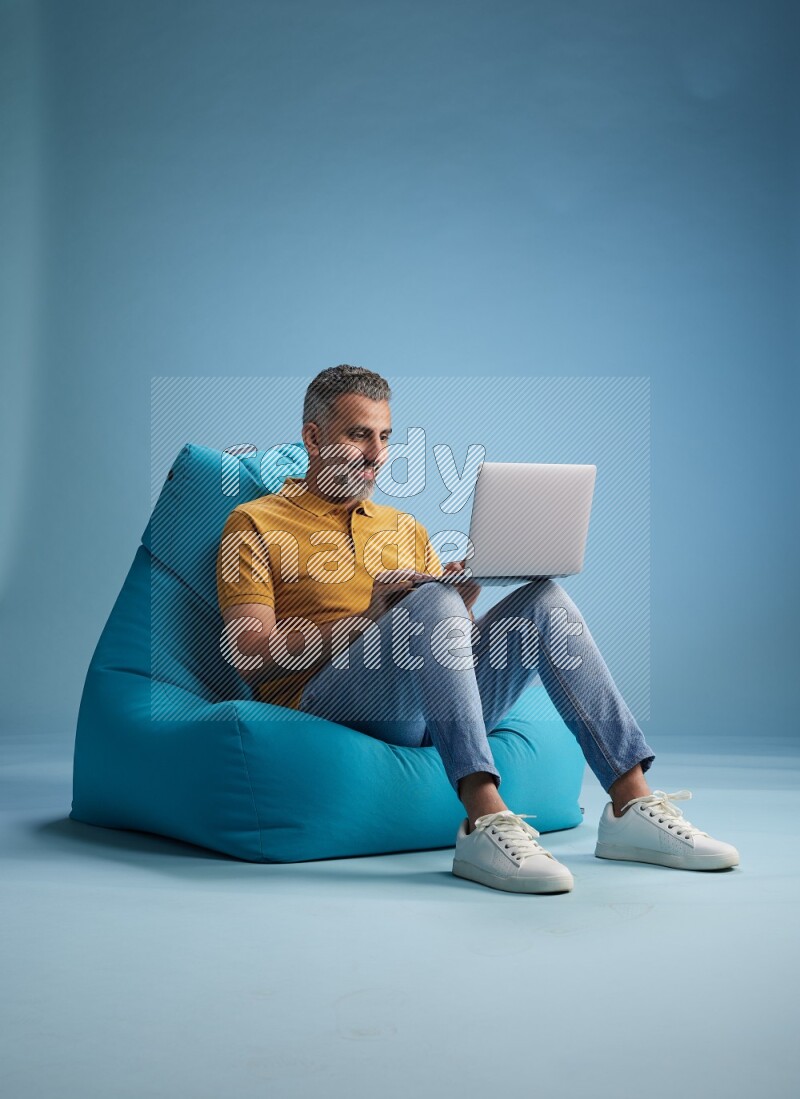 A man sitting on a blue beanbag and working on laptop