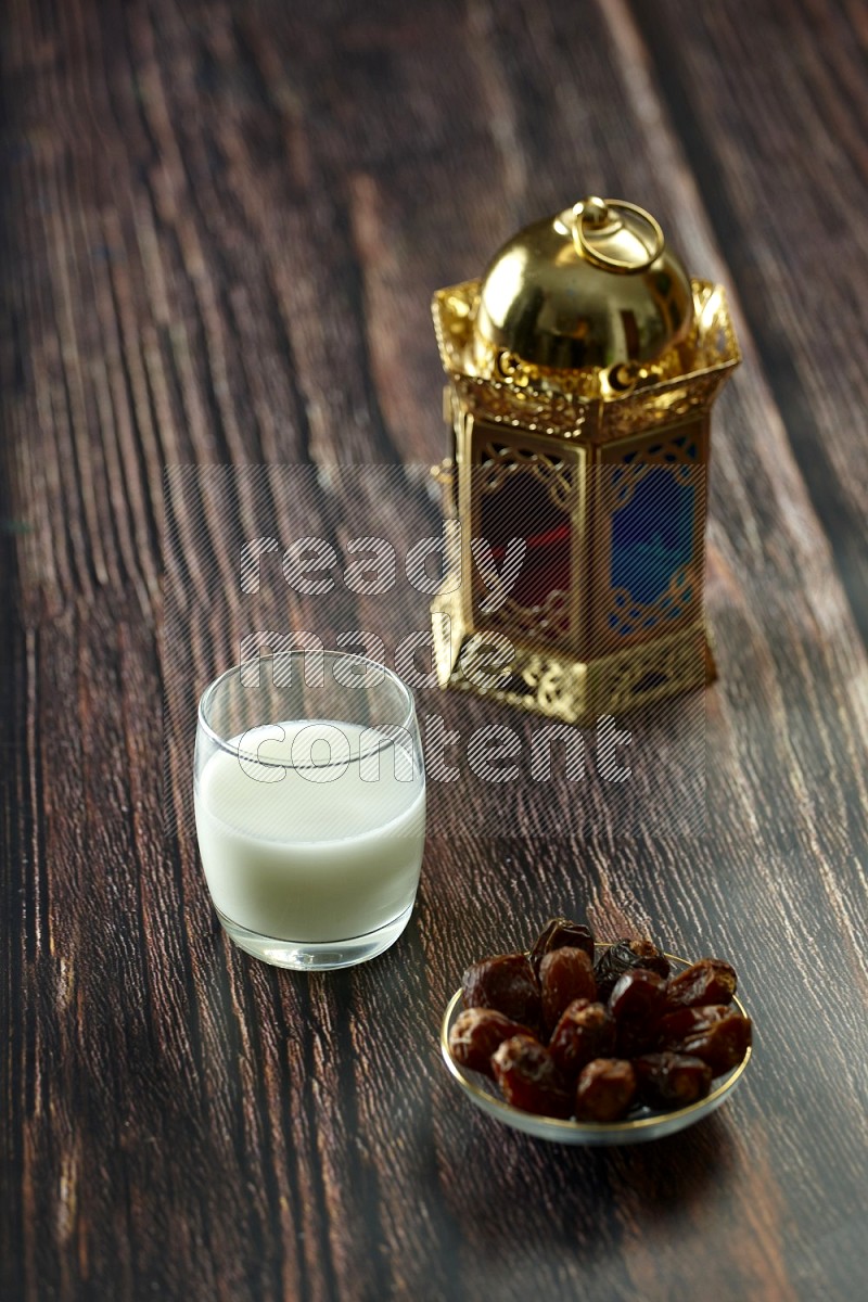 A golden lantern with drinks, dates, nuts, prayer beads and quran on brown wooden background