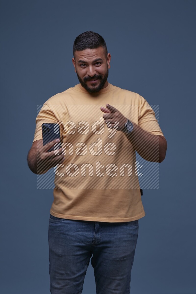 A man Pointing at a Smartphone on Blue Background wearing Orange T-shirt