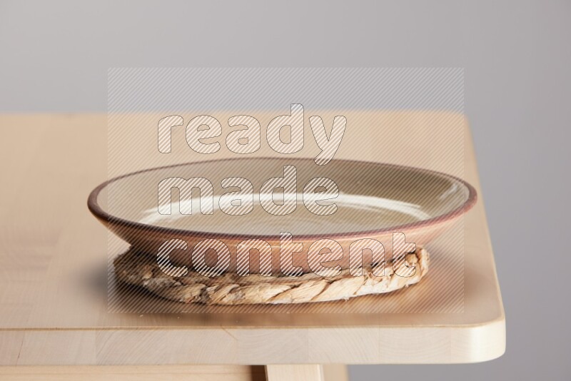 multi-colored pottery Plate placed on a small light colored straw placemat on the edge of wooden table
