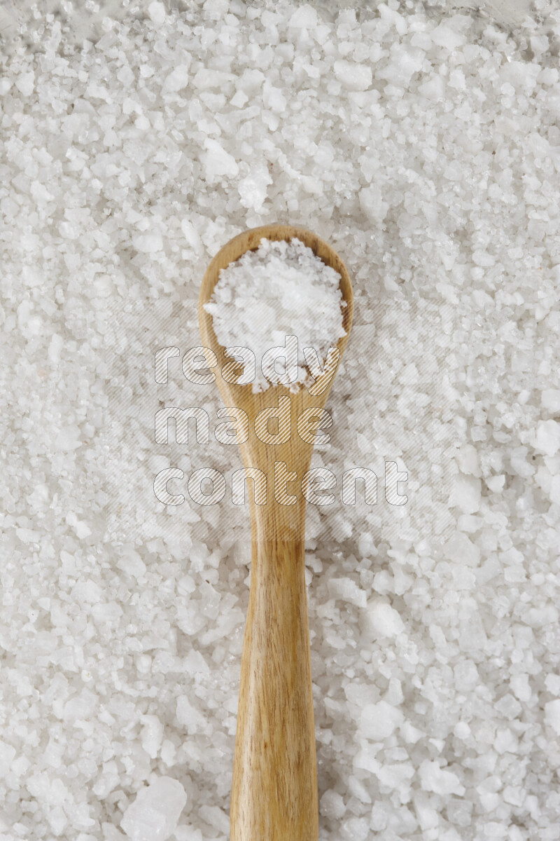 A wooden spoon full of white salt on white background