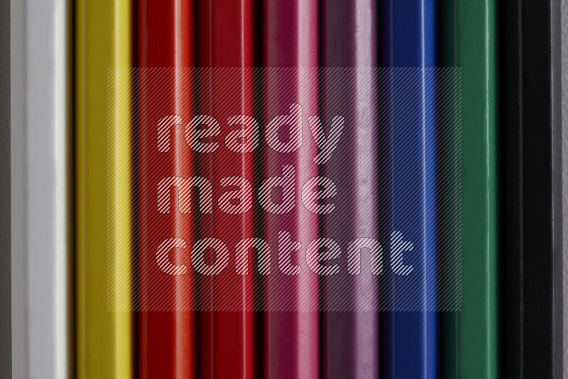 A collection of colored pencils arranged showcasing a gradient of different hues on grey background