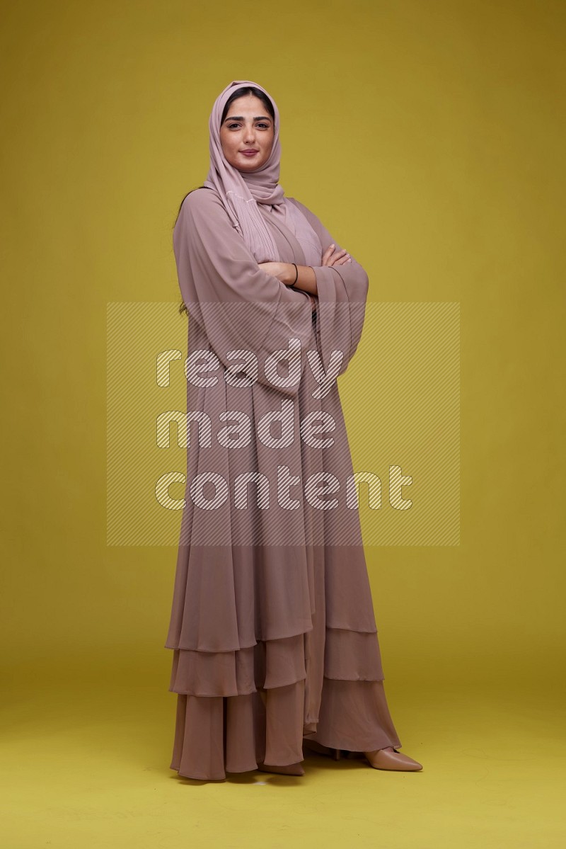 A woman Posing on a Yellow Background wearing Brown Abaya with Hijab