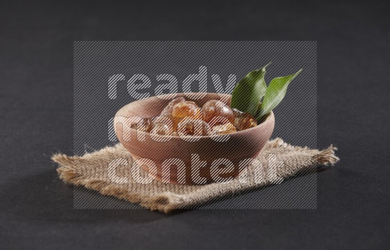 A wooden bowl full of gum arabic on a piece of burlap on black flooring