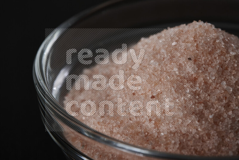 A glass bowl full of fine himalayan salt on black background