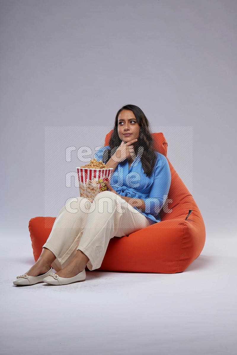 A woman sitting on an orange beanbag and eating popcorn