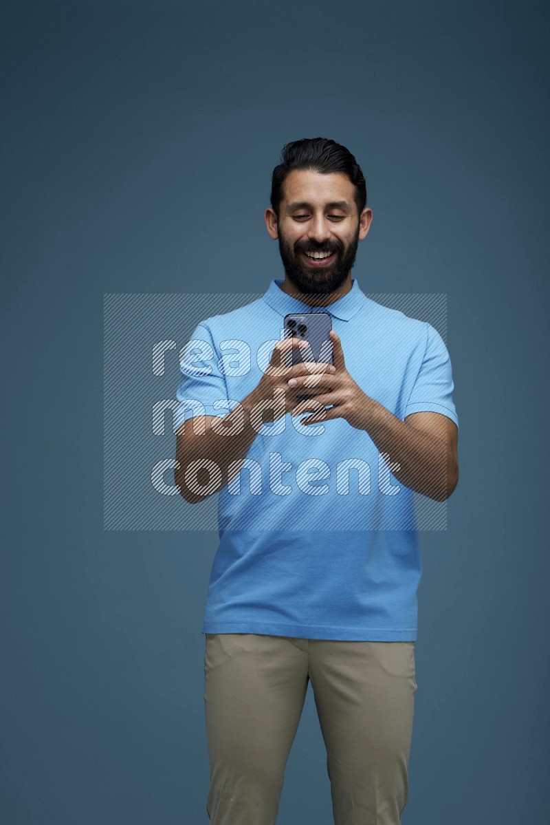 A man Texting on his phone in a blue background wearing a Blue shirt
