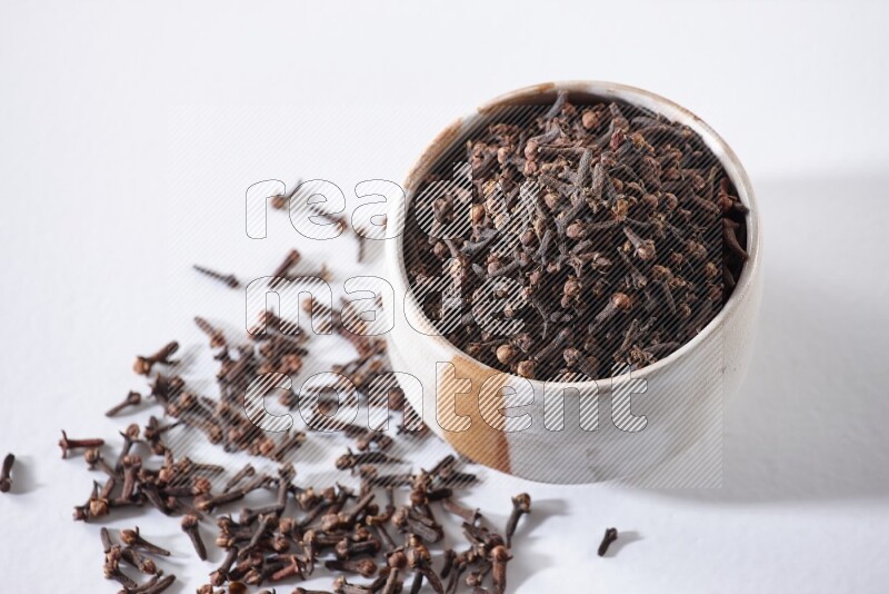 وعاء بيج من السيراميك ممتلئ بحبوب القرنفل علي خلفية بيضاء