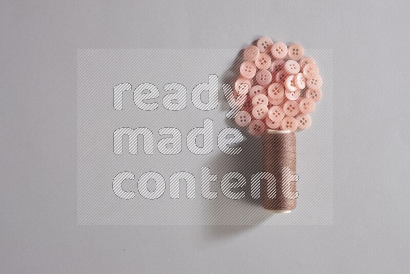 A brown sewing thread spool with colored buttons on grey background