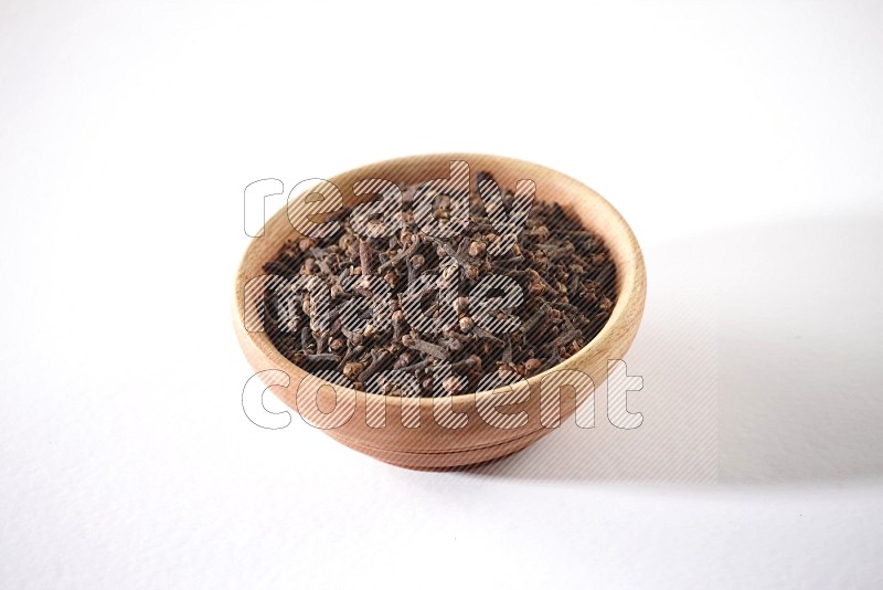 A wooden bowl full of cloves on a white flooring