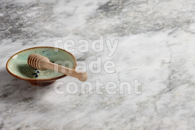 Decorative Pottery Plate with wooden honey handle in it, on grey marble flooring, 45 degree angle