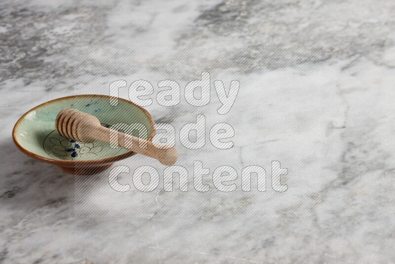 Decorative pottery plate with wooden honey dipper in it on grey marble background