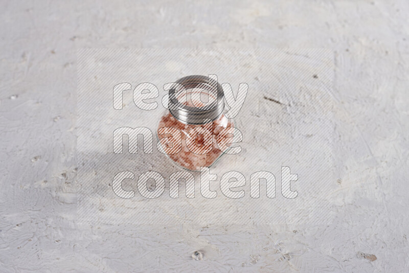 A glass jar full of coarse himalayan salt crystals on white background