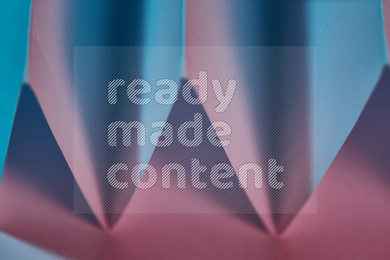 صورة مجردة مقربة تظهر طيات ورقية هندسية حادة بتدرجات اللون الأزرق والوردي