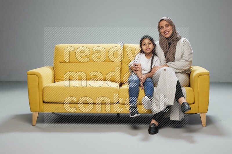 A girl with her mother sitting and interacting with the camera on gray background