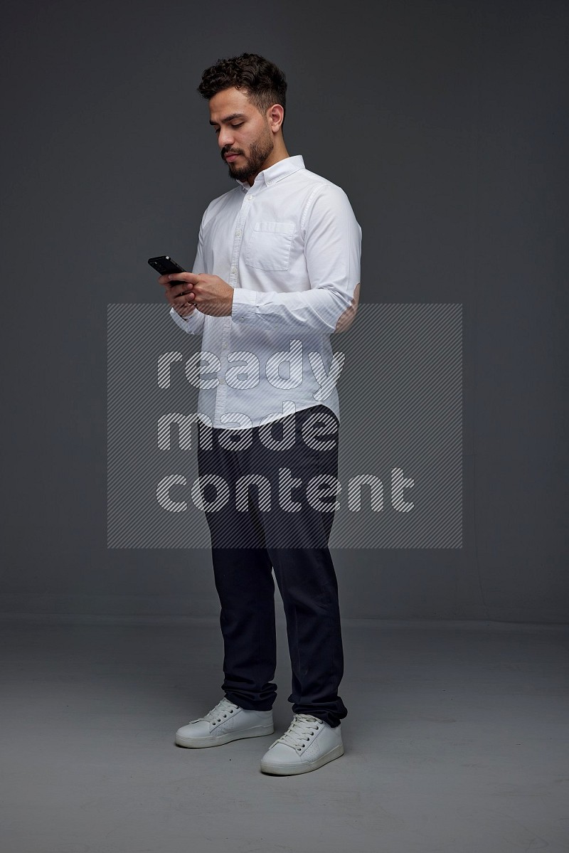 A man wearing smart casual standing and using his phone eye level on a gray background