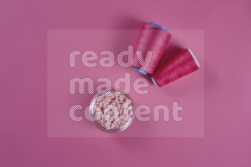 A pink collection of sewing and tailoring tools arranged on a pink background