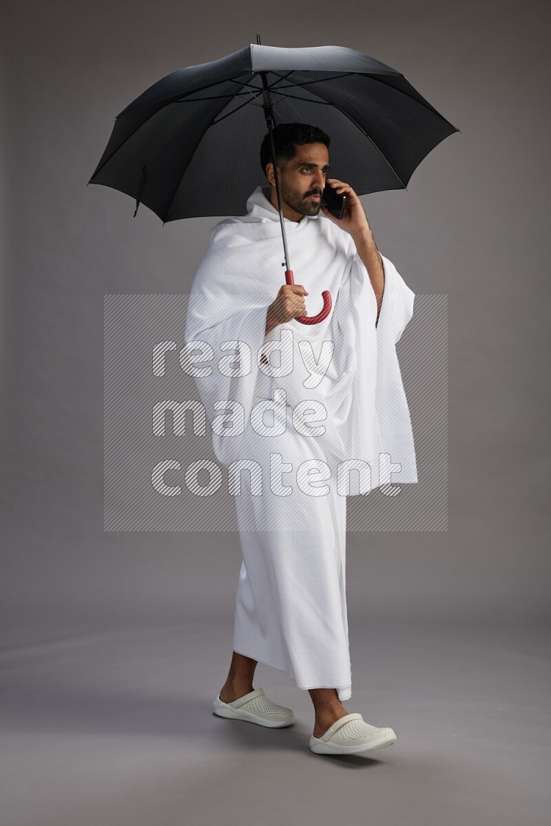 A man wearing Ehram Standing holding umbrella on gray background