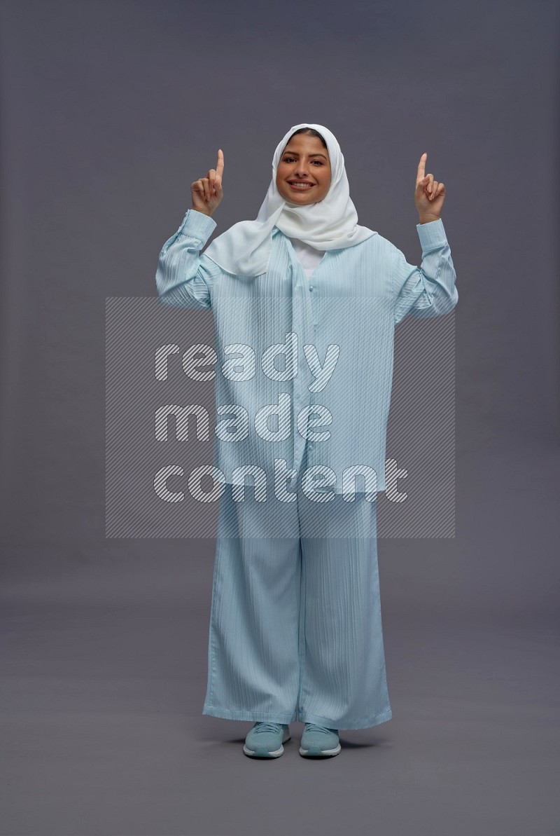 Saudi woman wearing hijab clothes standing interacting with the camera on gray background